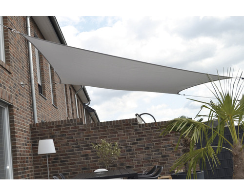 Driehoekig schaduwdoek boven een terras met bakstenen muur en tuinmeubelen