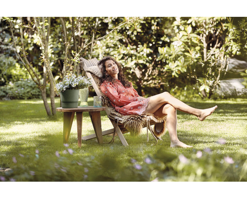 Vrouw ontspant in de tuin op een ligstoel naast een bijzettafel met bloemen en een glas.