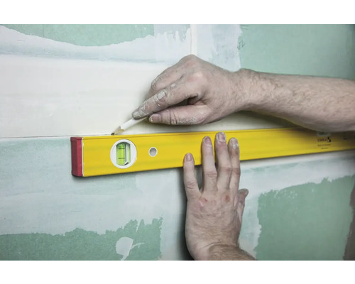 Een waterpas wordt gebruikt om een lijn op een muur te markeren.
