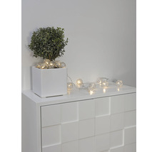 Decoratieve lichtketting met bolvormige lampen op een witte commode naast een potplant.