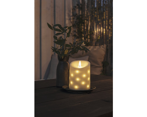 Decoratieve ledkaars met stippenpatroon op een tafel, naast een vaas met takken.