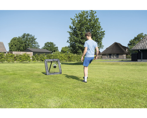Persoon speelt voetbal met een voetbaldoel in de tuin.