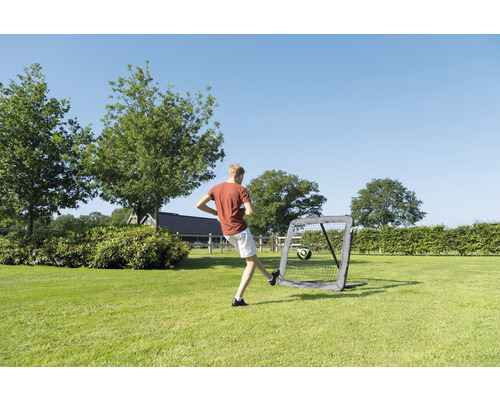 Jonge schiet voetbal in een draagbaar voetbaldoel in de tuin.