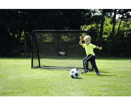 Jongen speelt voetbal voor een voetbaldoel in de tuin.