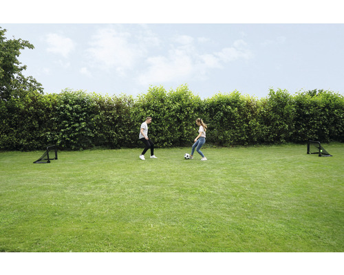 Twee mensen spelen met een voetbal op een gazon met twee voetbaldoelen.
