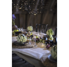 Feestelijk gedekte tafel met bolvormige lampen, servies, glazen en seizoensgroenten als decoratie.
