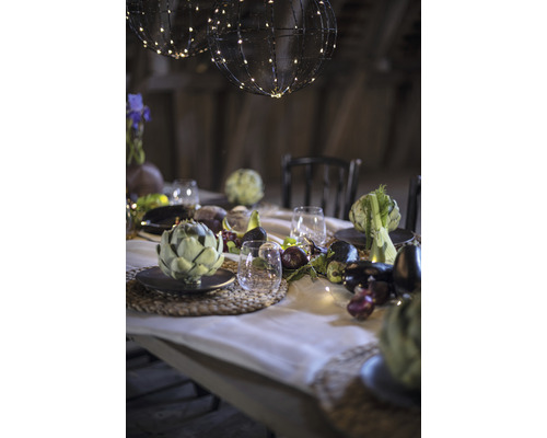 Feestelijk gedekte tafel met bolvormige lampen, servies, glazen en seizoensgroenten als decoratie.