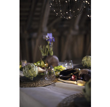 Decoratieve tafel met artisjokken, glazen, bloemenvaas en lichtjes onder bolvormige lampen.