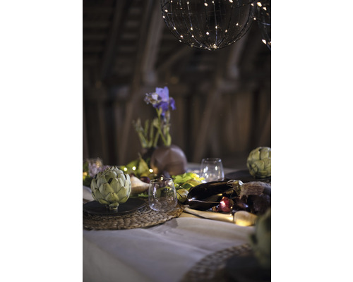 Decoratieve tafel met artisjokken, glazen, bloemenvaas en lichtjes onder bolvormige lampen.