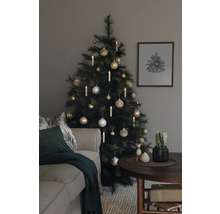 Kerstboom versierd met ballen en kaarsen naast een bank en een tafel