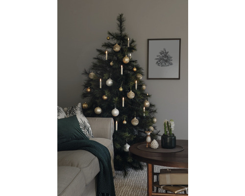 Kerstboom versierd met ballen en kaarsen naast een bank en een tafel