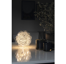 Decoratieve bolvormige tafellamp naast kaarsen en potplant op tafel