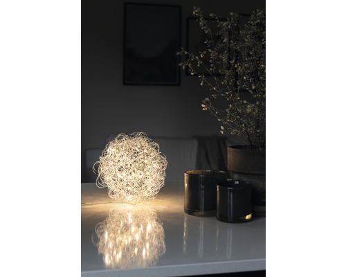 Decoratieve bolvormige tafellamp naast kaarsen en potplant op tafel