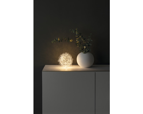 Decoratieve opstelling met een lichtgevende draadbal, een vaas en takken op een kast.