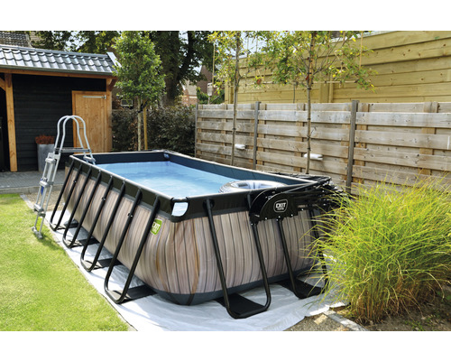 Rechthoekig zwembad met houten bekleding, ladder en filterpomp in de tuin.