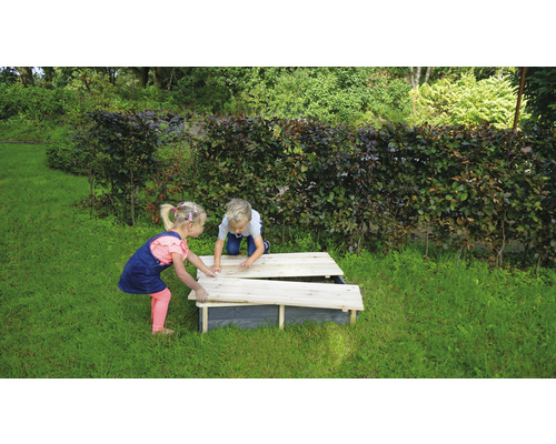 Twee kinderen spelen met een zandbak met deksel in de tuin.