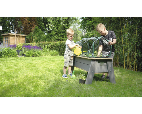 Twee kinderen bewateren en beplanten een verhoogde kweekbak met broeibak in de tuin.