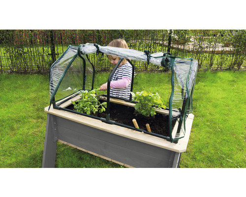 Hoge plantenbak met broeibak en kind dat in de tuin tuiniert.