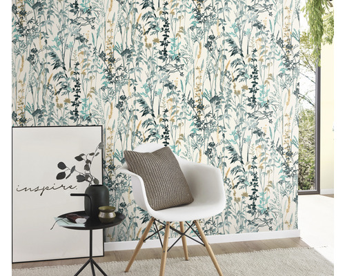 Een kamer met een bloemenbehang in blauwgroene en beige tinten, een witte stoel met kussen, een bijzettafel met decoratie en een schilderij.