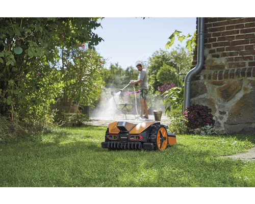 Robotmaaier op gazon, op de achtergrond reinigt iemand een terras met een hogedrukreiniger
