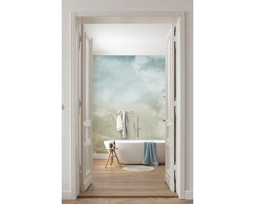 Lichte badkamer met ligbad, kruk en behang met wolkenpatroon, gezien door een open deur.