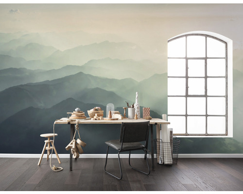 Een kamer met een fotobehang van een berglandschap, een bureau, een stoel en een raam.