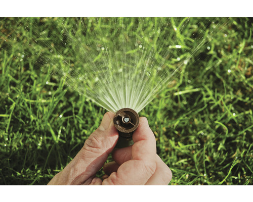 Een hand houdt een gazonsproeier vast die water sproeit.