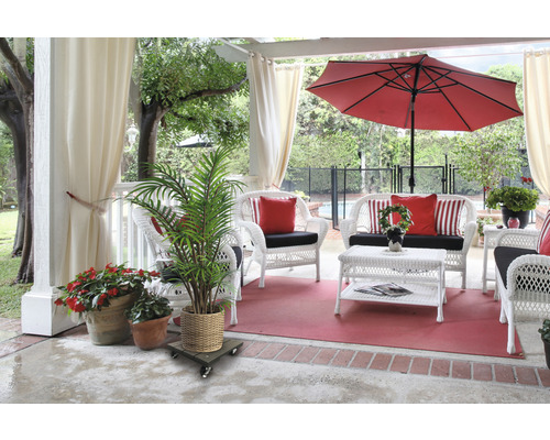 Terrasscène met witte rieten meubels, rode parasol en potplanten