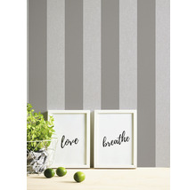Grijs gestreept behang met twee ingelijste kunstprints en een plant op een tafel