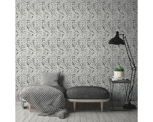 Een kamer met een bloemetjesbehang, een bank, een fauteuil, een vloerlamp en een bijzettafel