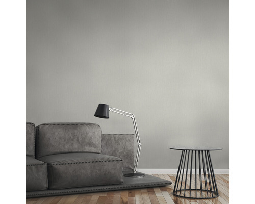 Woonkamer met grijze bank, vloerlamp en bijzettafel voor een effen muur