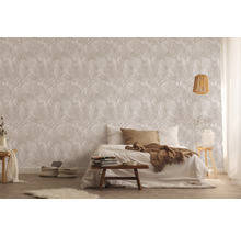Slaapkamer met bed voor een wand met bladpatroonbehang.