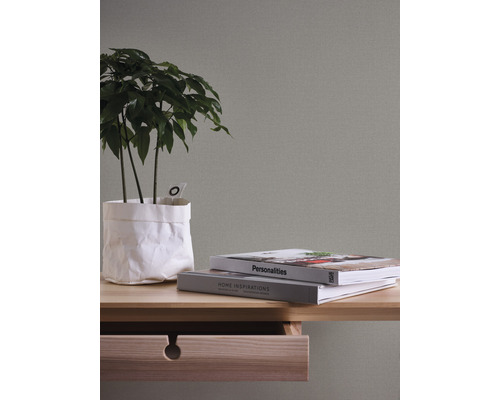 Close-up van een tafel met plant, boeken en open lade tegen een gestructureerde wand