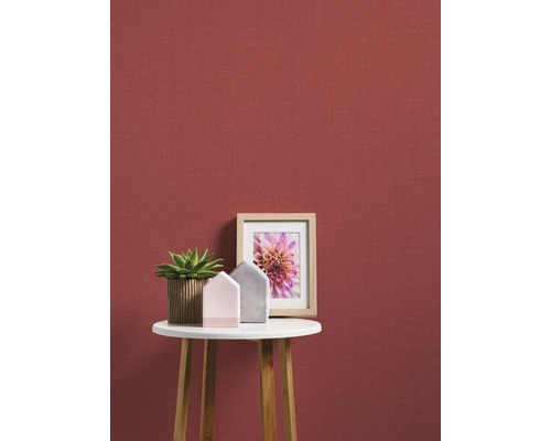 Decoratieve scène met plant, decoratiehuisjes en fotolijst op een bijzettafel tegen een rode wand