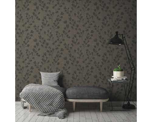 Een woonkamer met een patroonbehang, een kruk, een fauteuil en een vloerlamp.