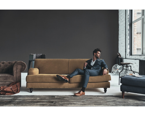 Woonkamer scène met bank, fauteuil, kruk en stijlvol geklede man