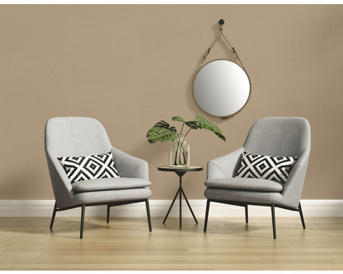 Twee grijze fauteuils met kussens, een bijzettafel met een vaas en een plant, en een ronde spiegel tegen een wand.