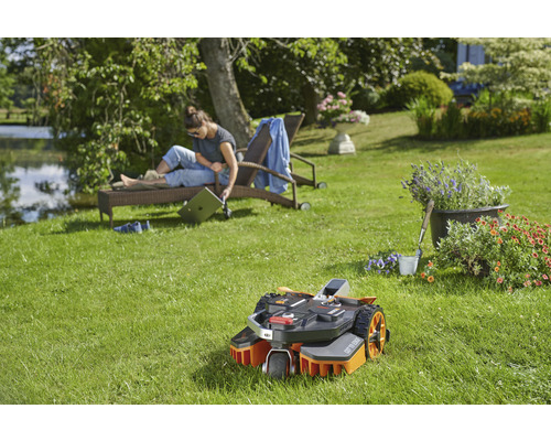 Scene met een gazonrobot op een groen gazon, terwijl een vrouw ontspant op een ligstoel