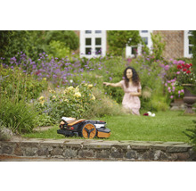 Robotmaaier in een bloeiende tuin, terwijl een vrouw zich tot de bloemen wendt