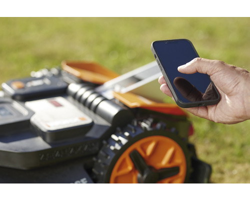 Een man bedient een robotmaaier met een smartphone.