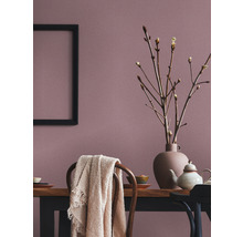 Eetkamer met houten tafel, serviesgoed, vaas met takken, deken op stoel en een zwart frame aan de wand.