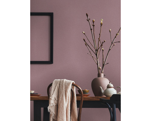 Eetkamer met houten tafel, serviesgoed, vaas met takken, deken op stoel en een zwart frame aan de wand.