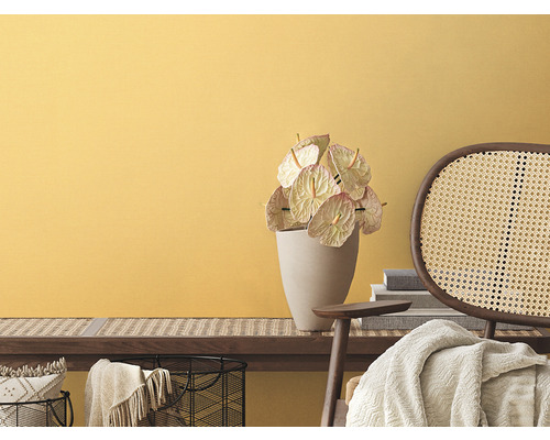 Woonkamer met gele muur, bank met rotan vlechtwerk, anthuriums in vaas en rotan stoel