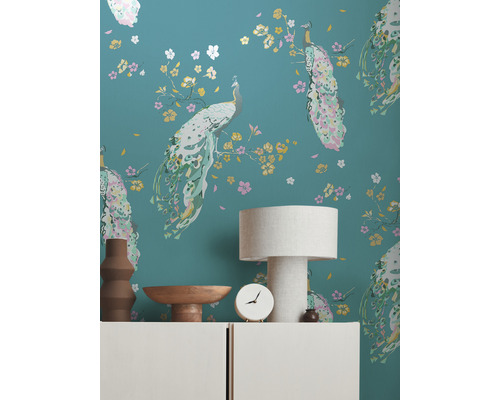 Wand met pauwenbehangpatroon, versierd met lamp, schaal, klok en vaas op een dressoir.