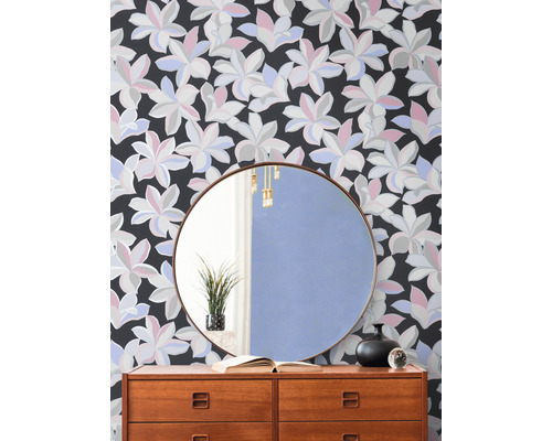 Decoratief interieur met een ladekast tegen een bloemenbehang en een ronde spiegel.