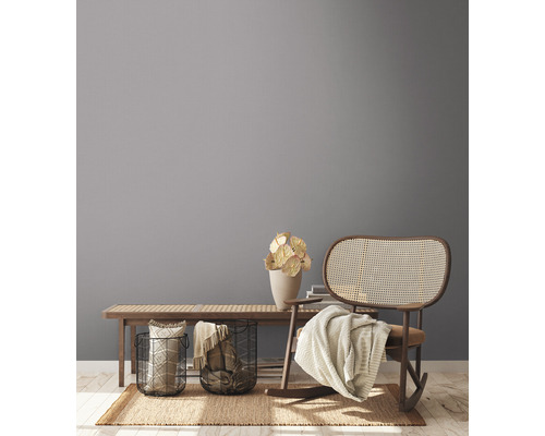 Woonkamerscène met houten bank, decoraties, manden en een schommelstoel op een tapijt.