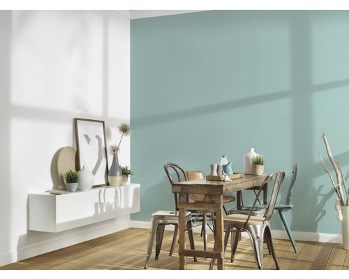 Eetkamer met houten tafel, stoelen en wandplank met decoraties tegen een gekleurde muur