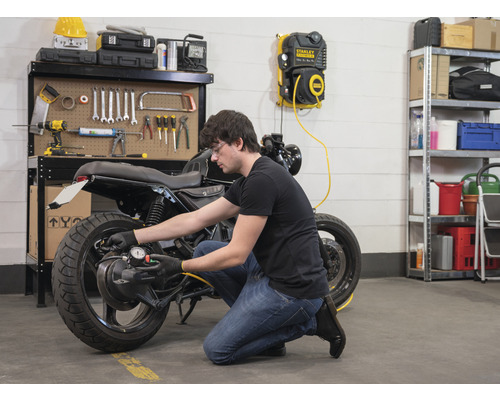 Man controleert bandenspanning van een motorfiets met luchtcompressor in werkplaats