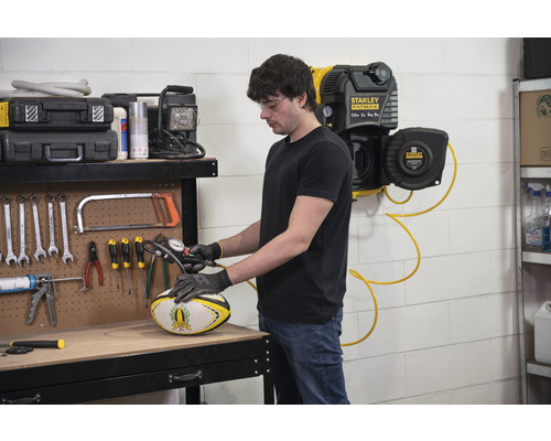 Een man pompt een rugbybal op met een compressor in een werkplaats.