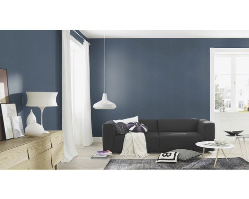 Woonkamer met bank, dressoir, lamp en decoratie voor een donkerblauwe muur